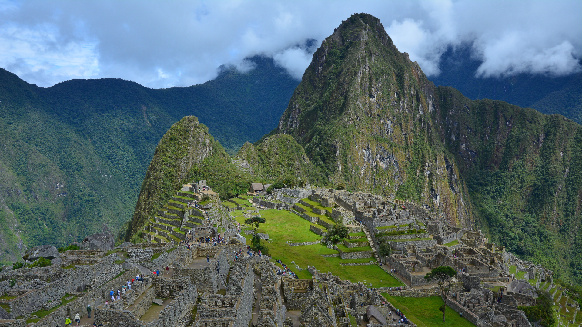 Panoramic view of the ancient Inca city of Machu Picchu, showcasing stone ruins, terraced fields, and Huayna Picchu mountain in the background.