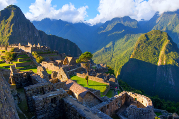 Ancient Inca citadel of Machu Picchu illuminated by morning sunlight, surrounded by lush green mountains under a clear sky.